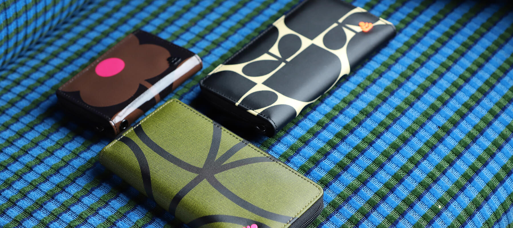 three colourful Orla Kiely wallets on a blue background