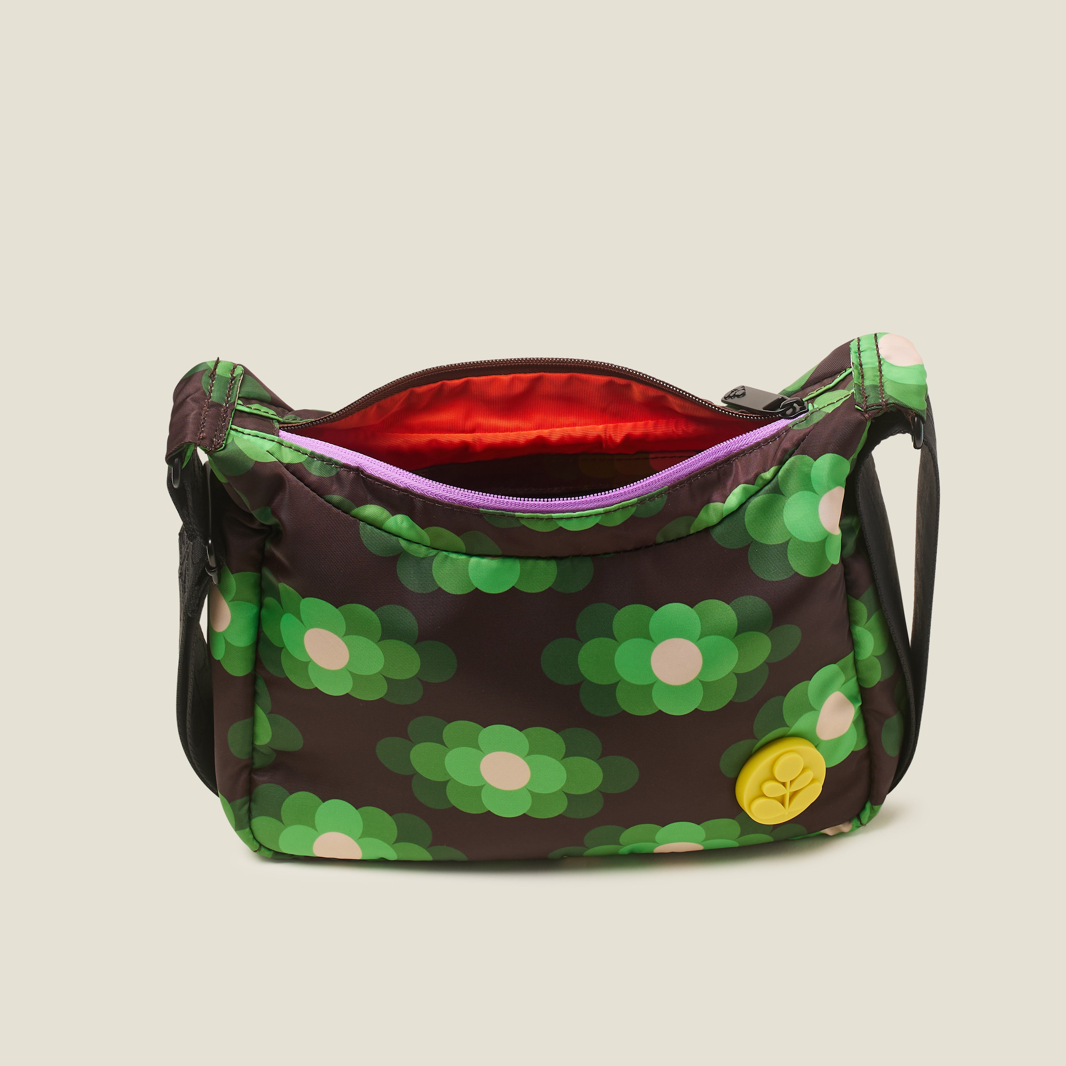 A view of the small crossbody hobo bag with the zipper open to reveal the orange lining, in our neon. green pattern with yellow stem logo branding.