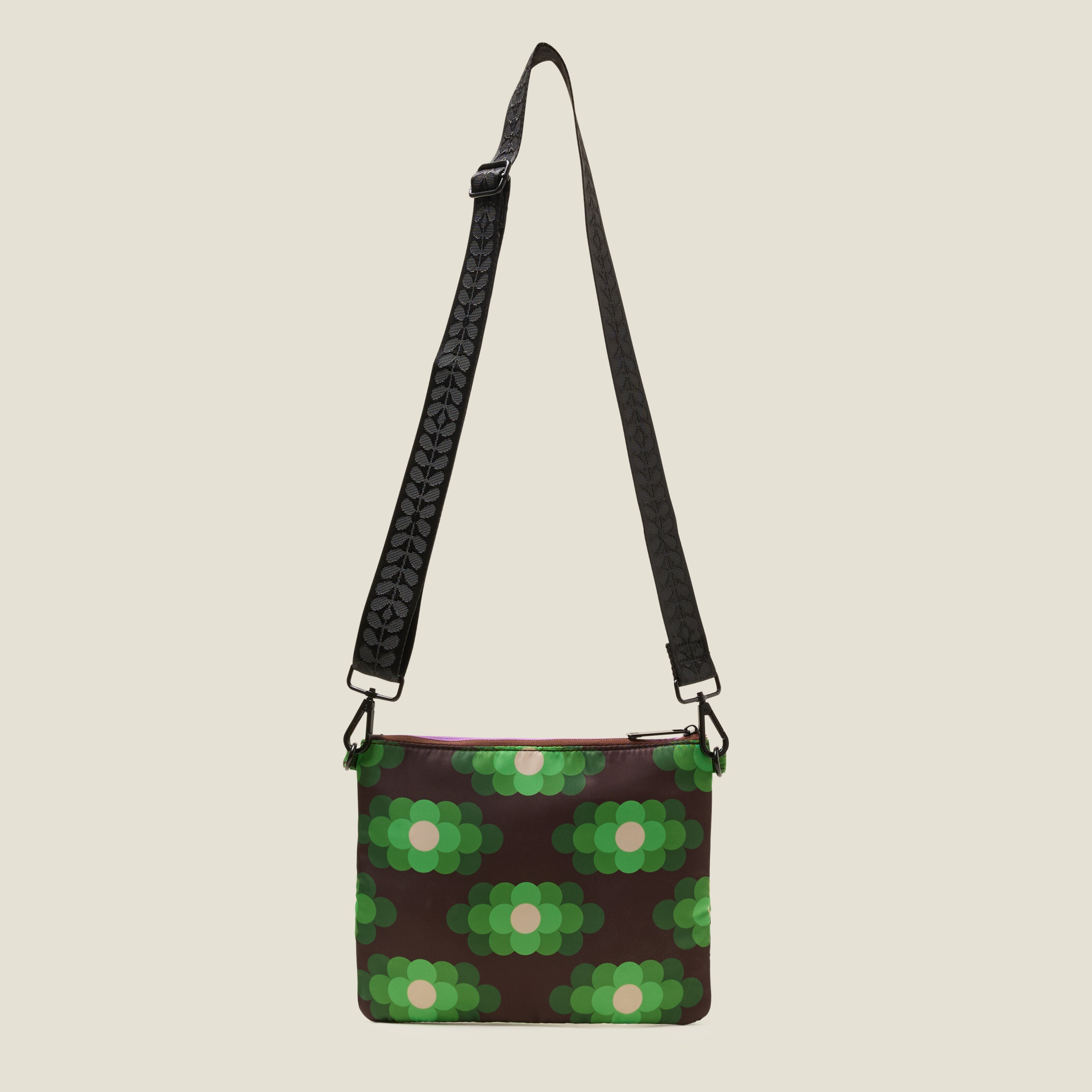 Green, brown and cream retro flower printed bag with a black strap on a beige background