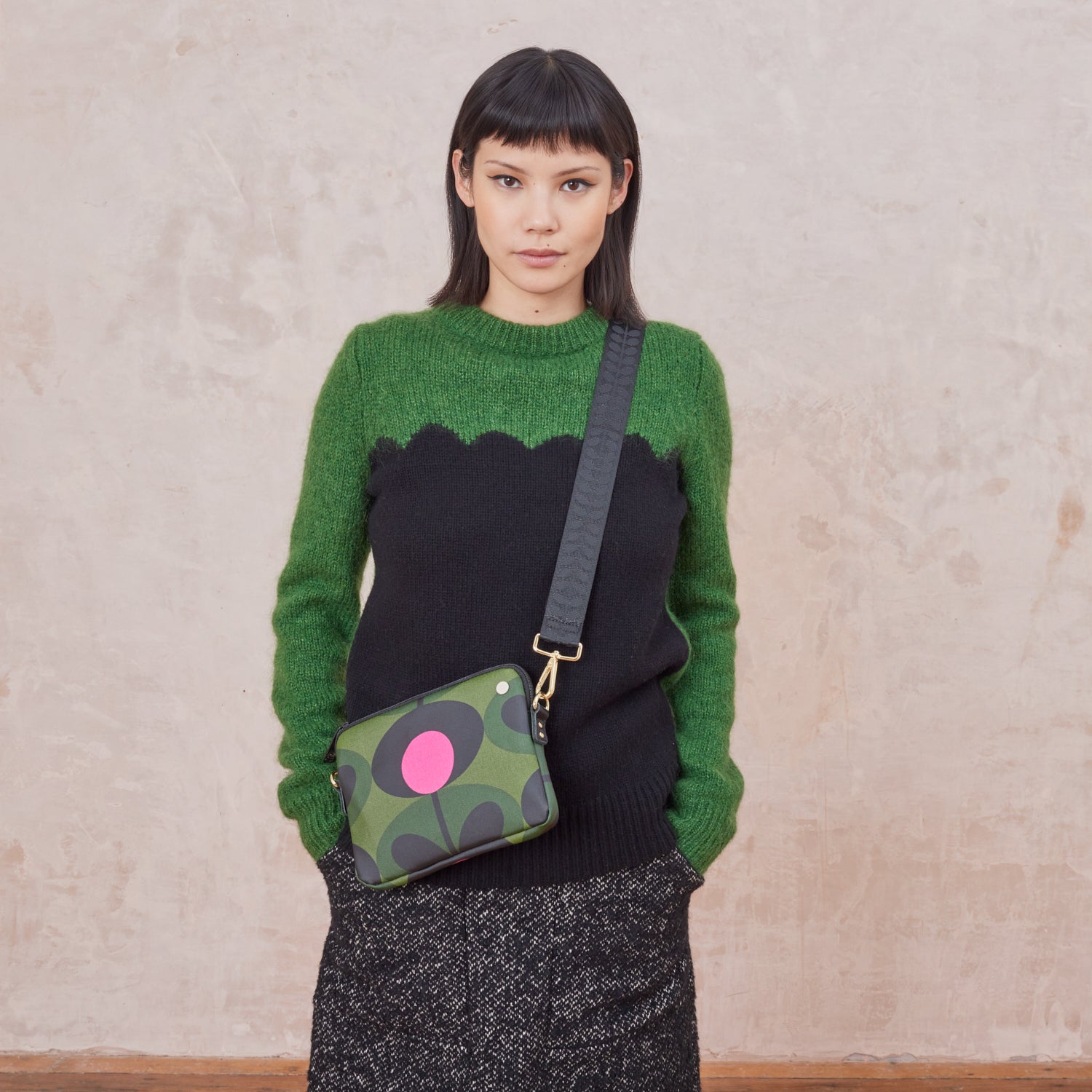 Woman wearing a green and black sweater holding a green patterned bag with pink spots
