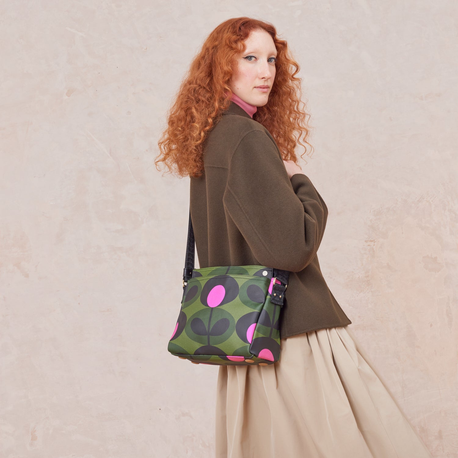 Woman wears the Fielder Crossbody bag - a green handbag with pink floral print
