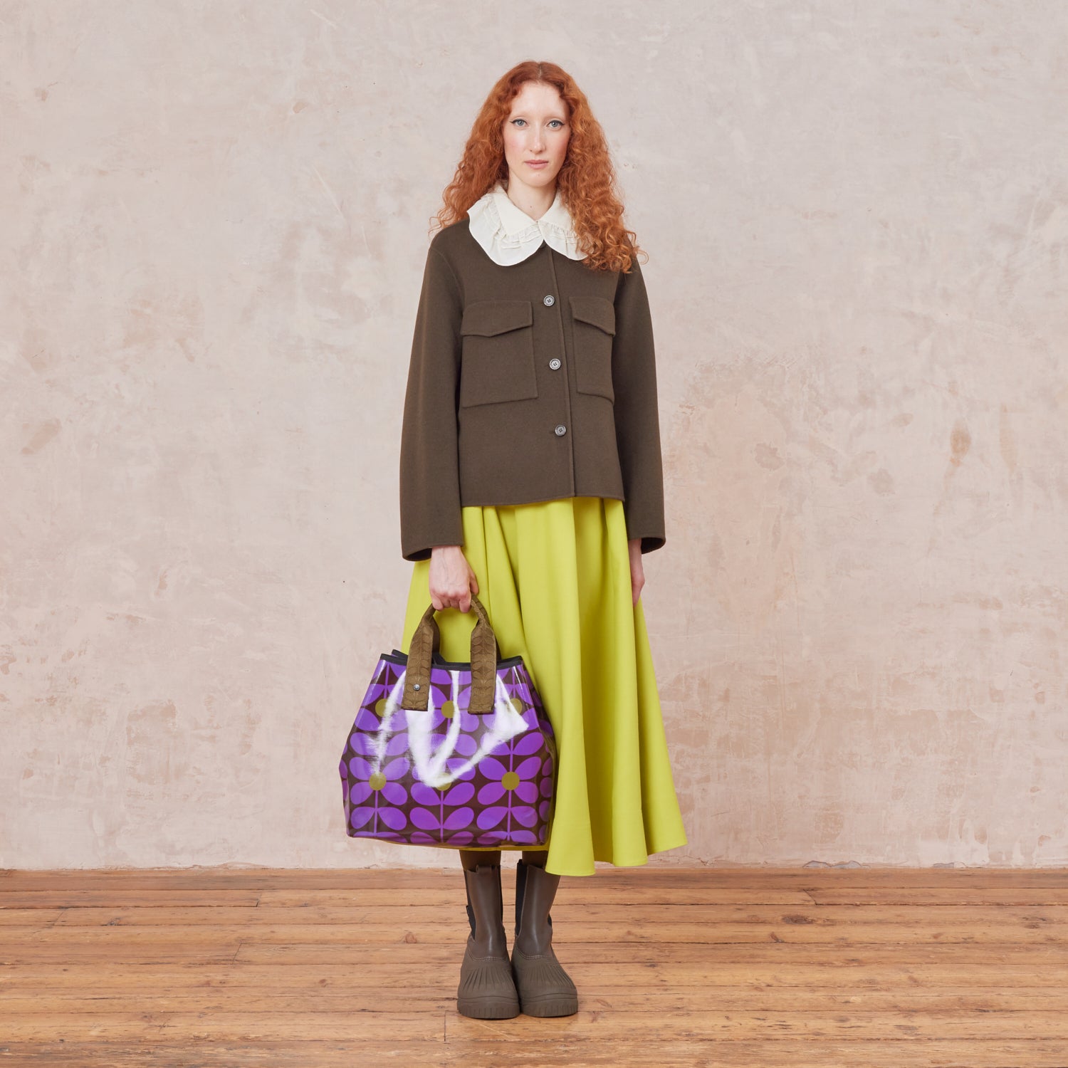 Woman holding a large patterned tote bag in purple, brown and green floral; stem print by the short grab handles.