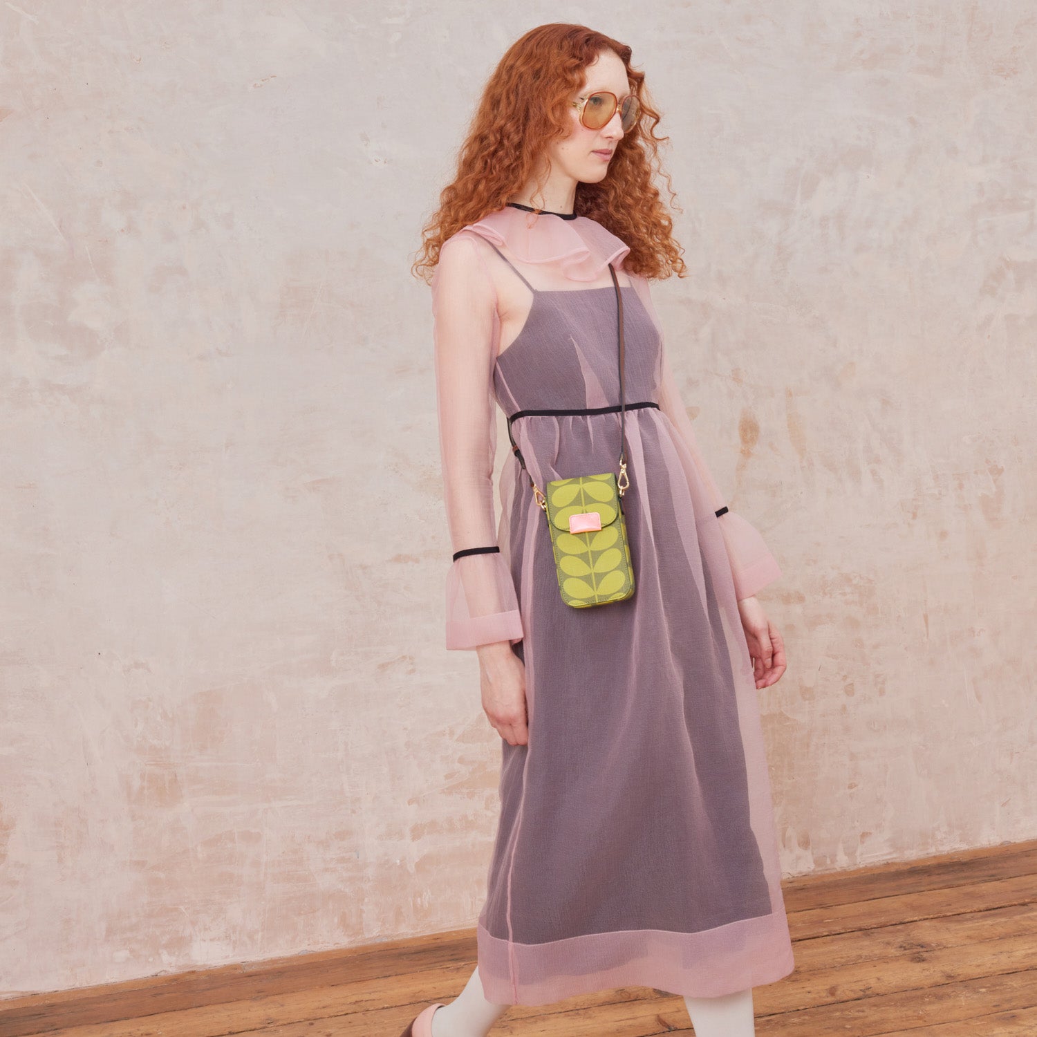 A woman in a pink sheer dress wears a green stem print phone pouch with leather crossbody strap.