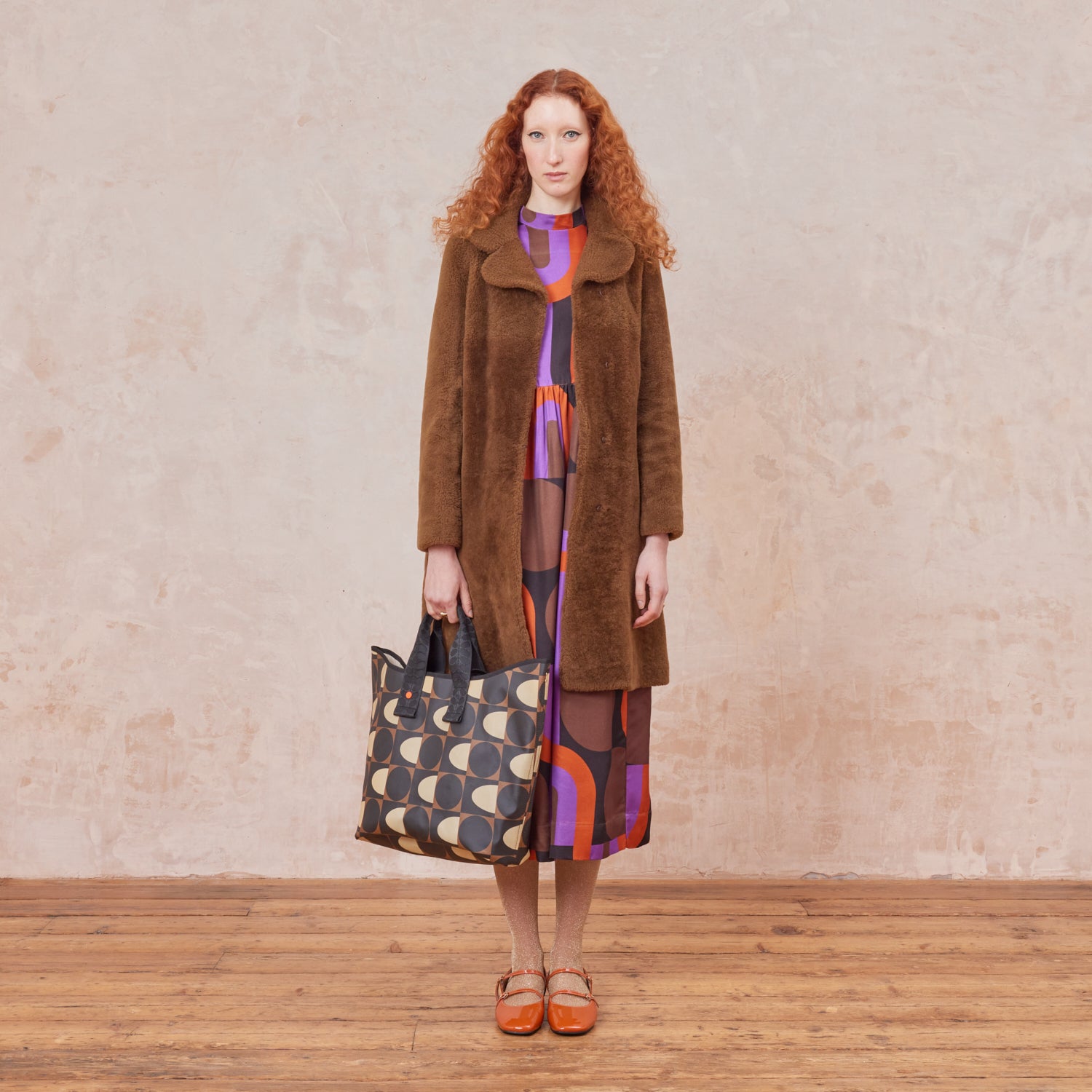 A woman holding a patterned tote bag with black, brown and beige spot square printed design.