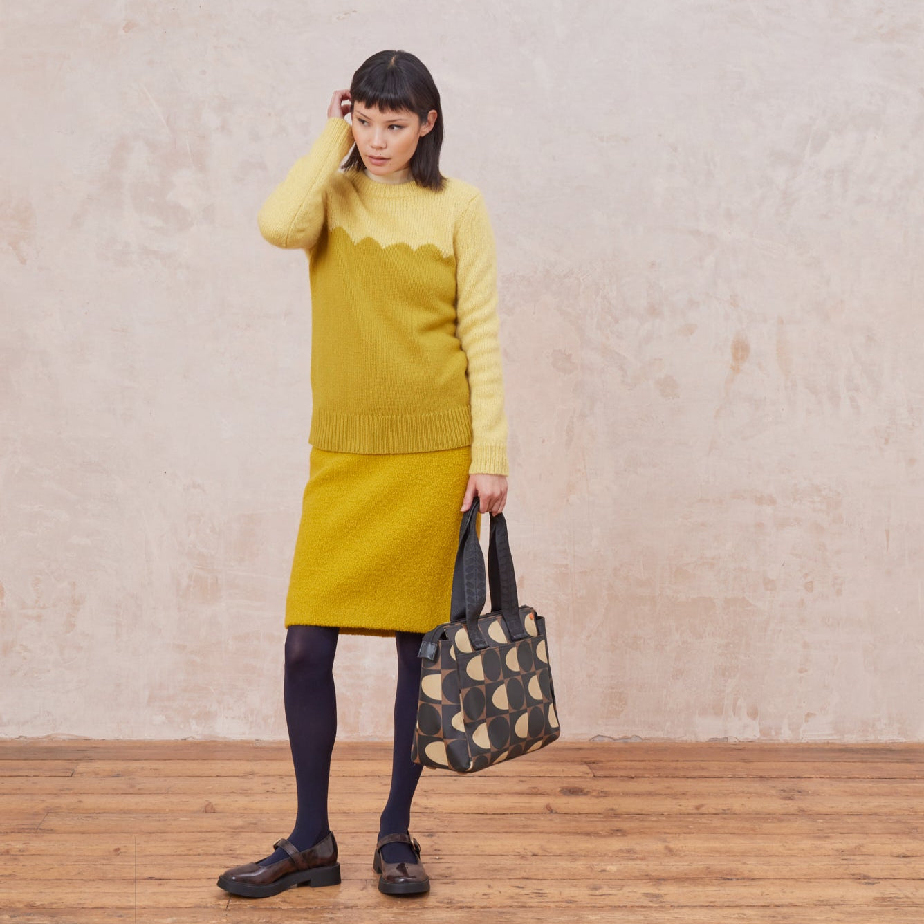 Woman in a yellow dress carrying a brown, black and cream patterned tote bag by its branded grab handles