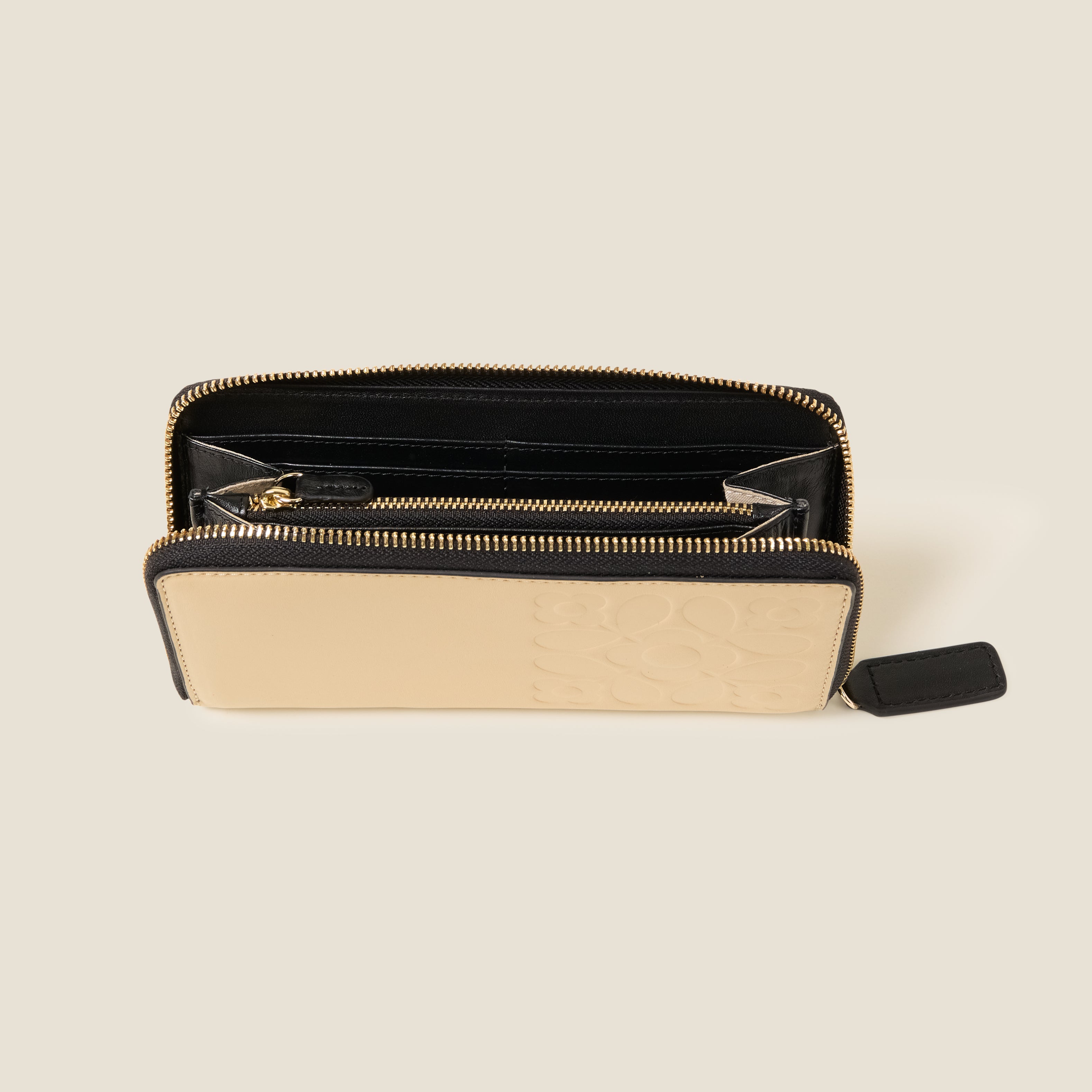 Top open view of a cream leather wallet with black zipper, featuring an Orla Kiely embossed pattern and internal pockets and card slots.