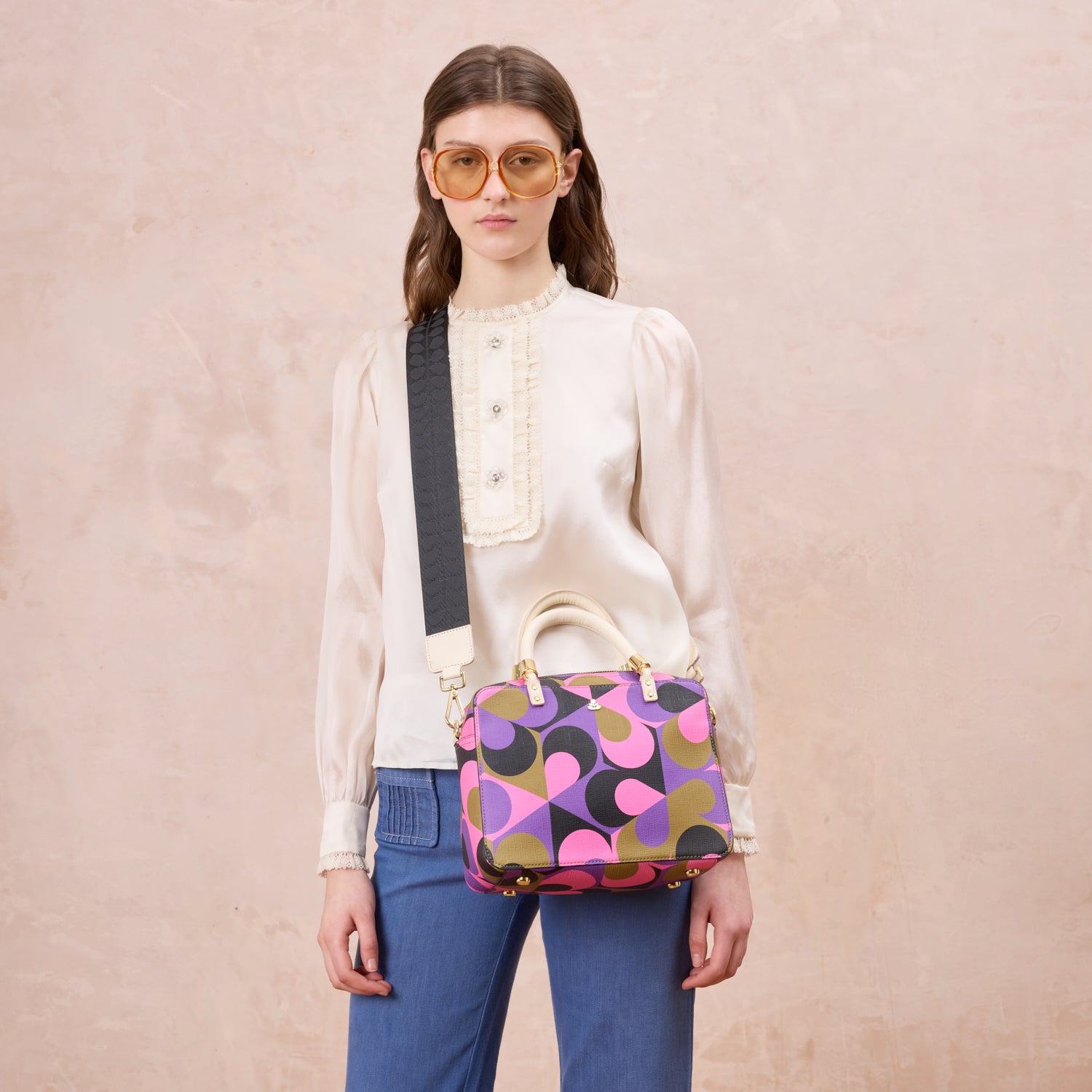 A women wears the medium square handbag with a purple pattern across her body, also featuring leather grab handles.