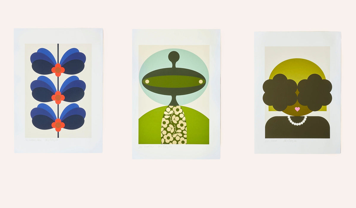 Three framed abstract art prints displayed side by side on a light beige wall. The left print shows blue and orange butterfly-like shapes; the center print shows a green and cream figure with a circular head; the right print shows a dark brown figure with a yellow circular background.