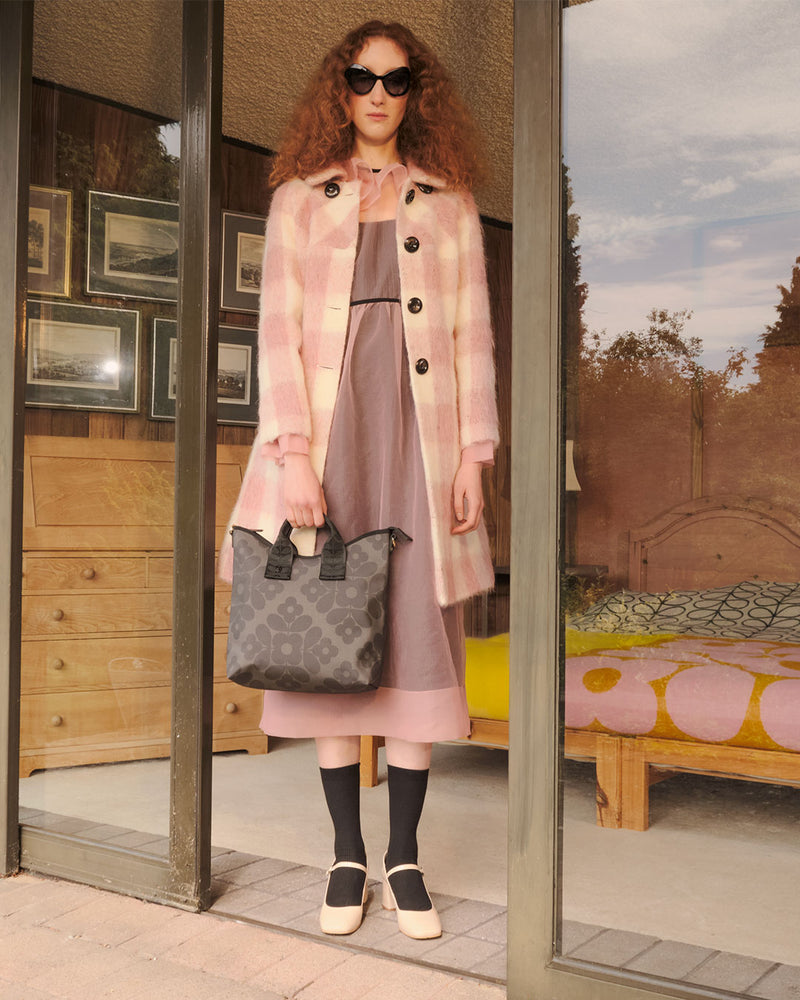 Woman wearing a pink gingham coat and a Flower Tile Orla Kiely bag