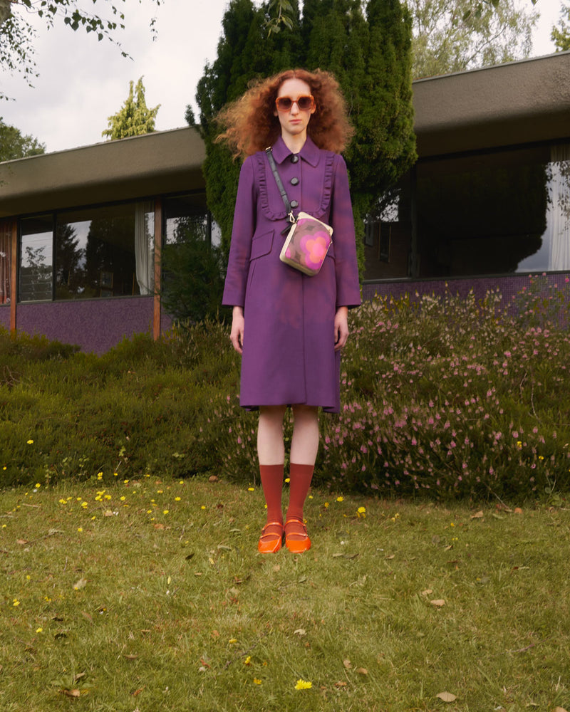 Woman standing in a garden wearing an Orla Kiely Portia leather crossbody bag