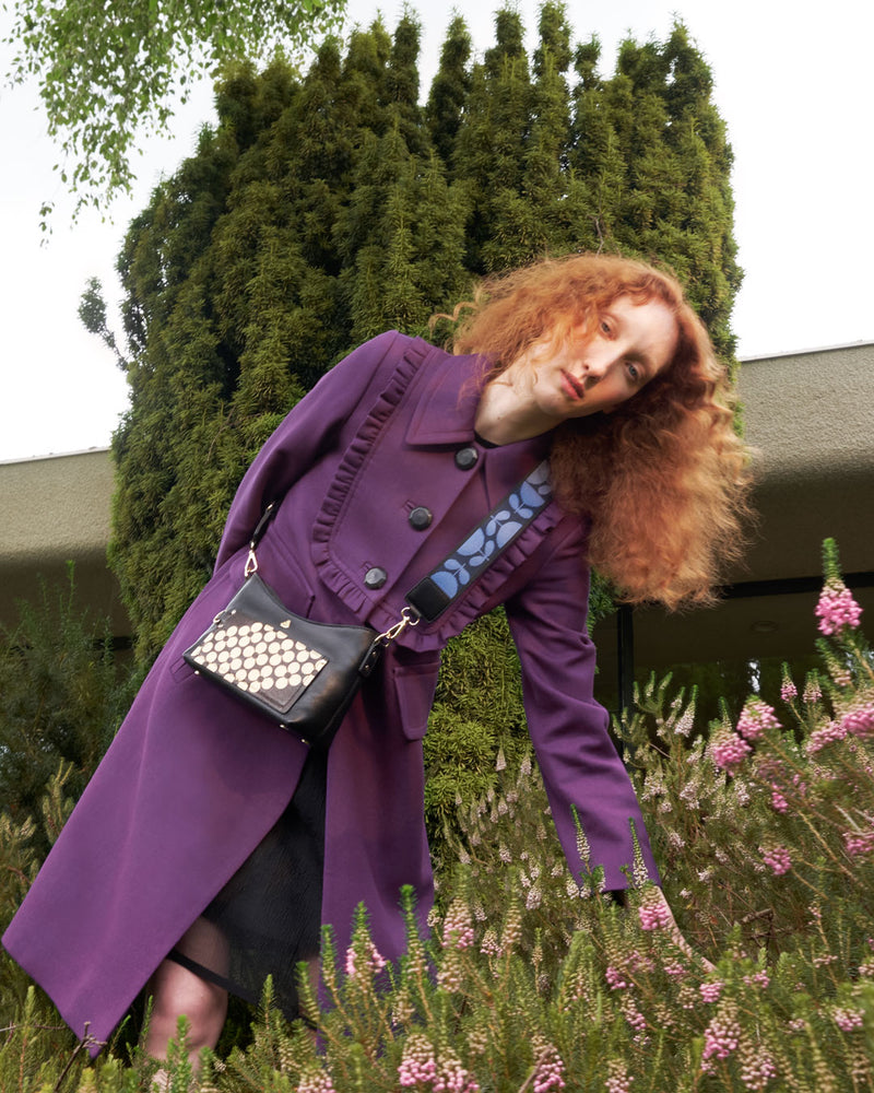 Woman standing amidst flowers wearing a floral leather Orla Kiely handbag