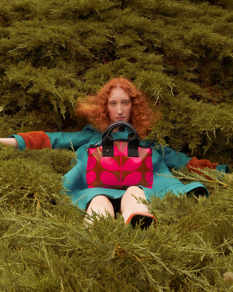person sitting in tree with pink Orla Kiely bag