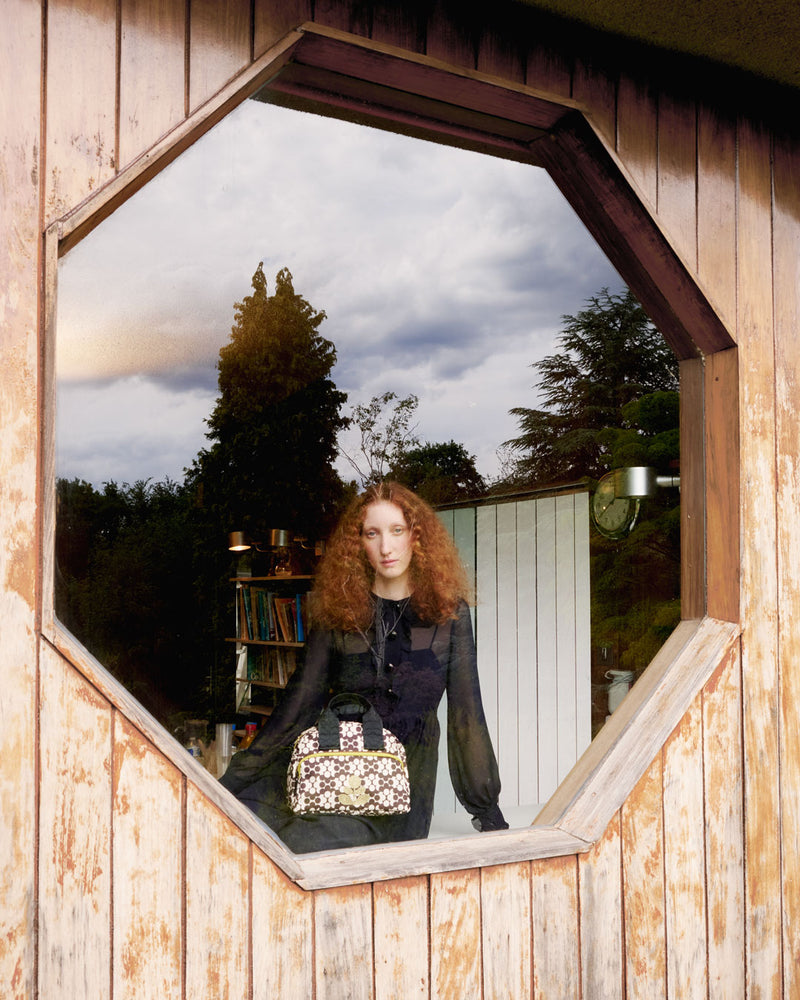 Model sat in a hexagonal window whilst wearing an Orla Kiely Radial handbag