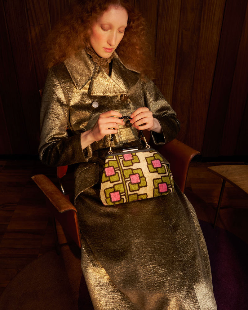 Model wearing sparkly gold coat and a velvet Orla Kiely handbag