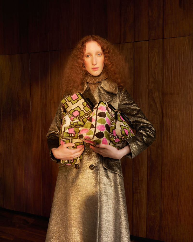 Model wearing gold sparkly trench whilst holding multiple velvet Orla Kiely handbags