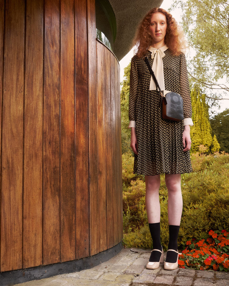 Women wearing an Orla Kiely punched leather Portia Crossbody in a garden