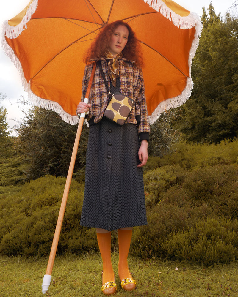 Woman holding orange parasol whilst wearing an Orla Kiely Portia Crossbody leather bag