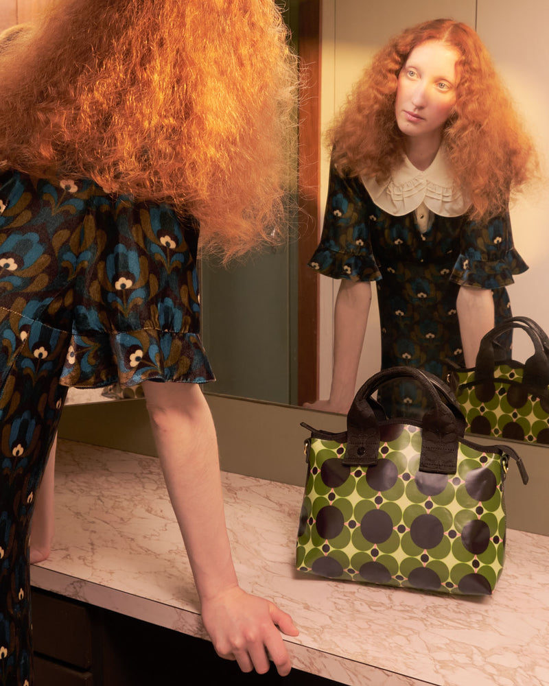 Model looking into a mirror with an Orla Kiely Hand Carry Handbag in shot