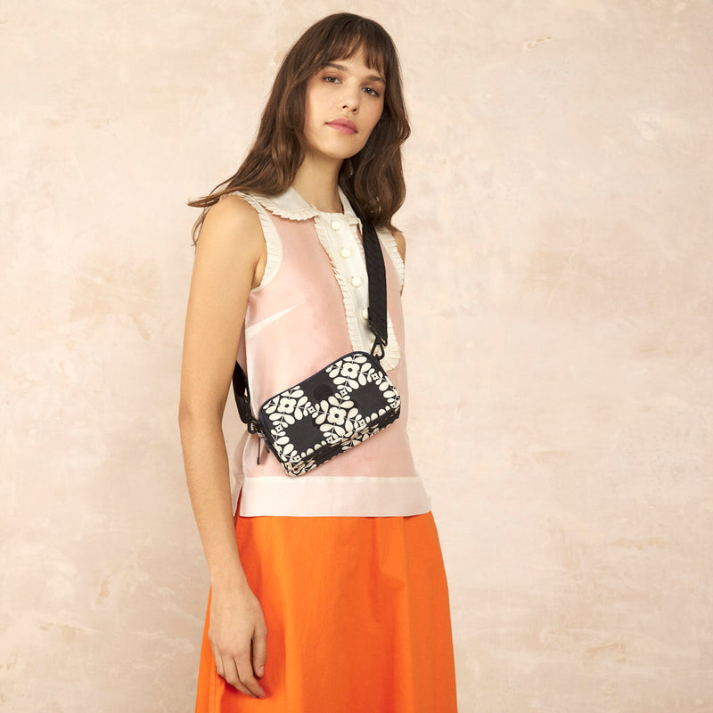 Model wearing the Tripod Crossbody in Lattice Flower Tile Onyx pattern by Orla Kiely