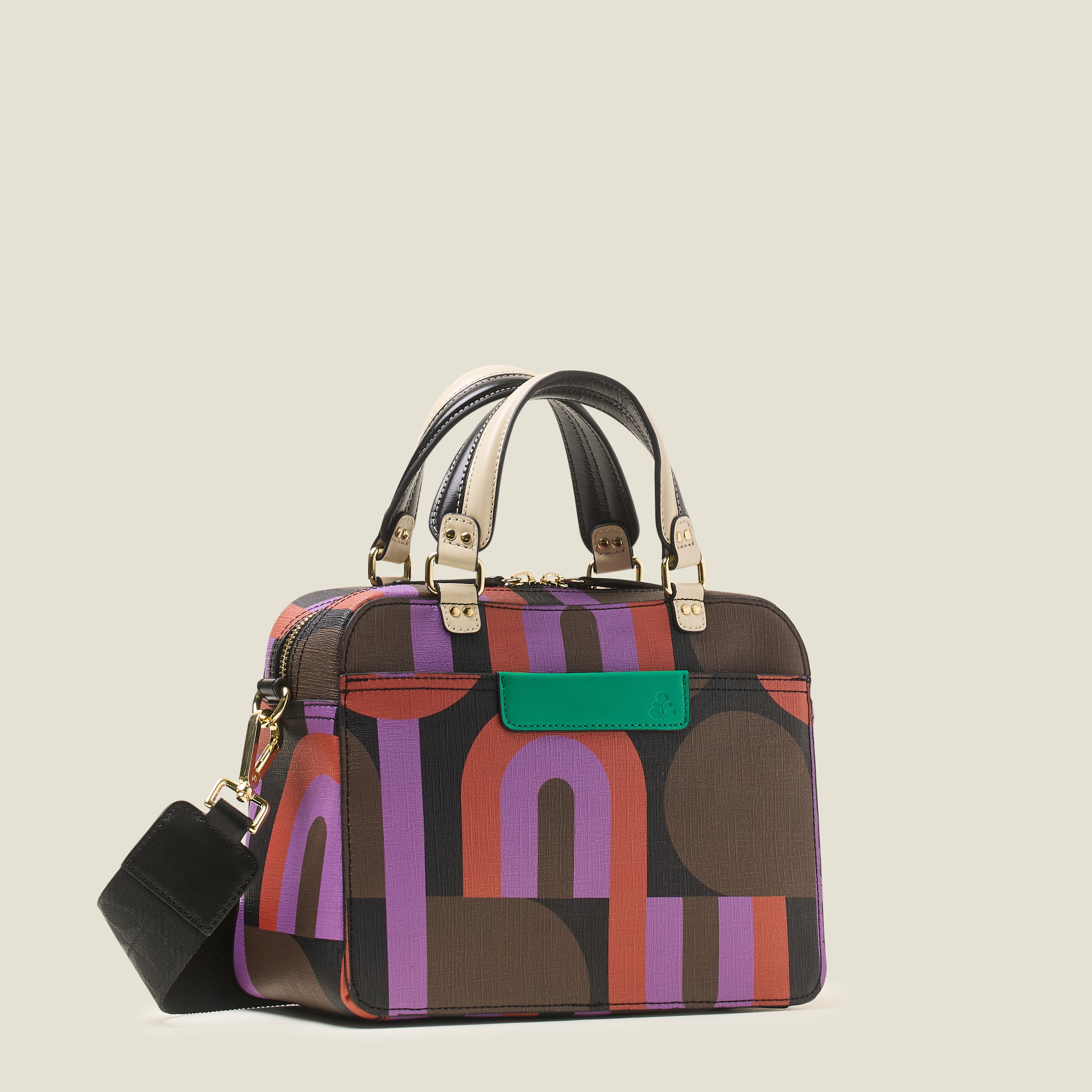 Side view of square shaped handbag in a retro purple, red and brown print, featuring grab handles, crossbody strap and zip closure.