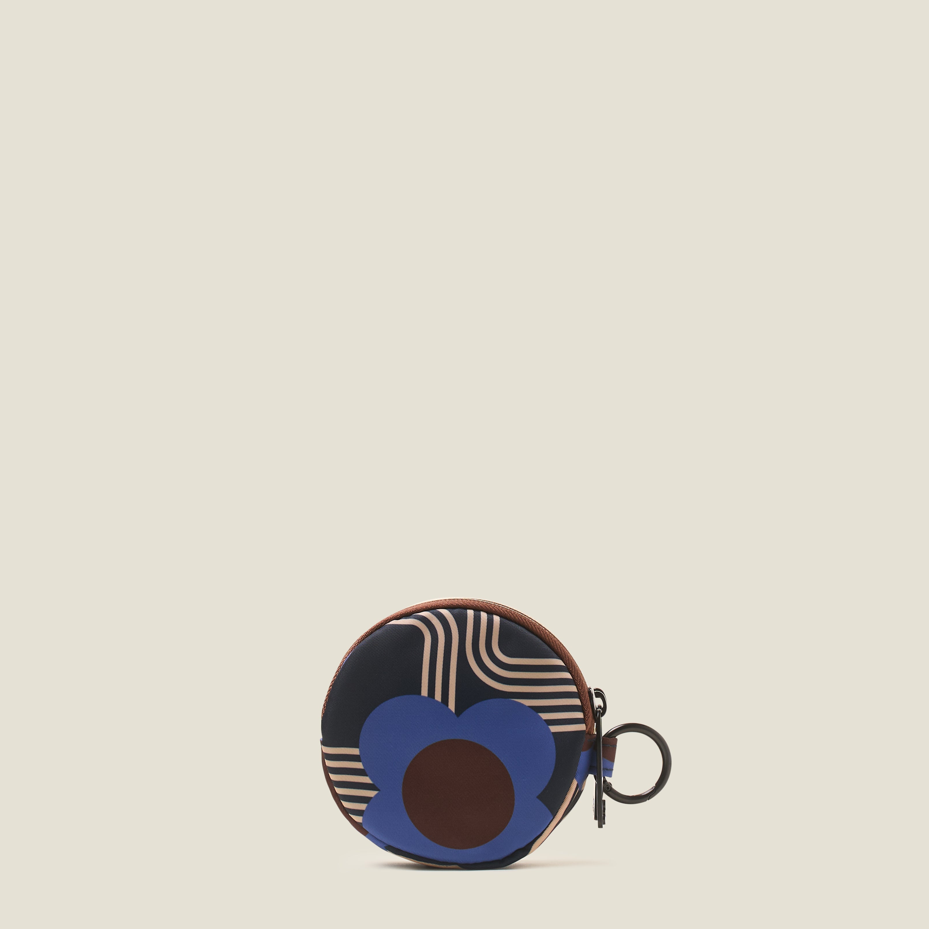 The back view of round change purse, with a rubber Orla Kiely stem logo on a blue, navy, brown and cream print with a ring clip on a beige background.