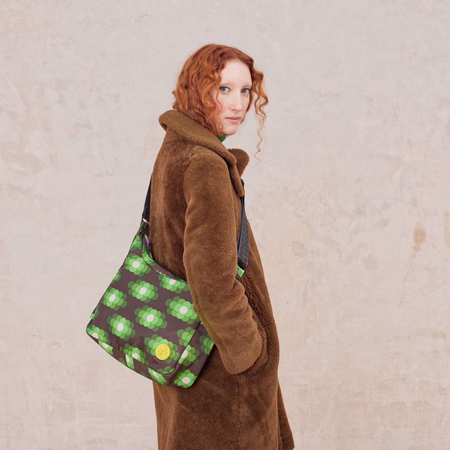 Woman wearing a crossbody bag in a neon green floral pattern. The handbag features a yellow stem logo detail.