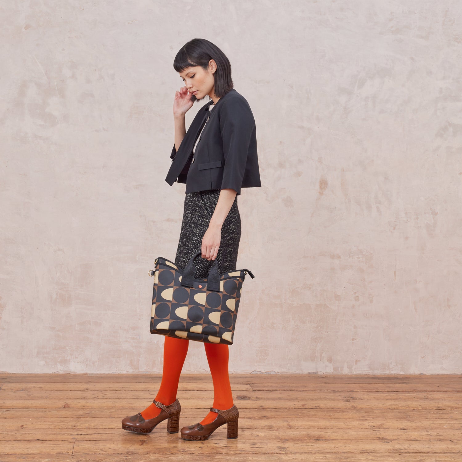 Women holding the bucket version by grab handles with front slip pocket in a geometric mocha brown print design 