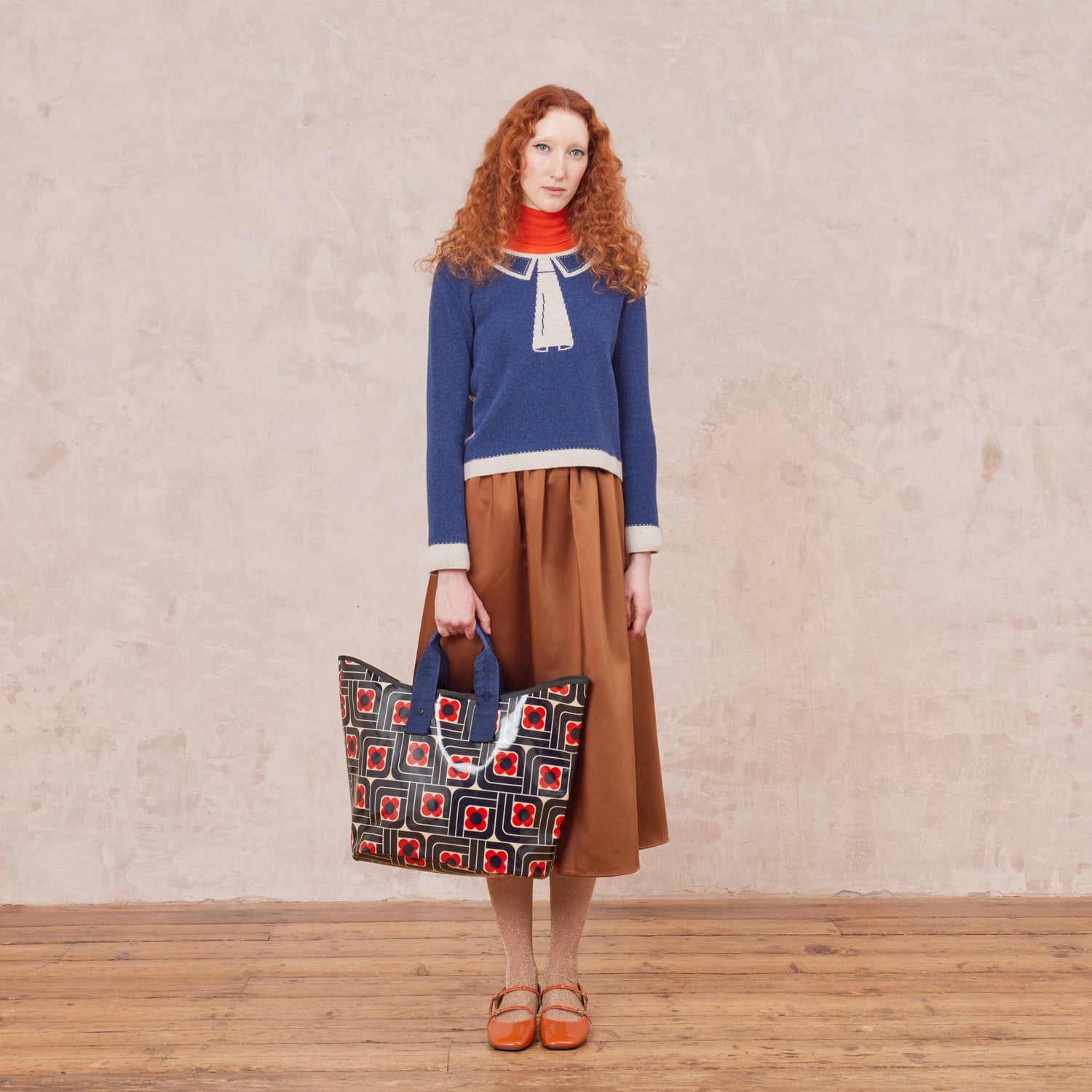 Woman holding a large patterned tote bag in navy red and cream woodblock print with two grab handles.