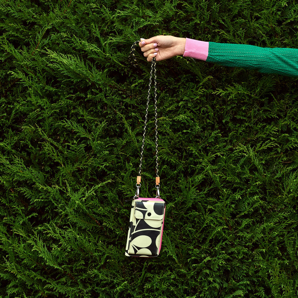 A keeper Orla Kiely phone pouch dangled in front of a hedge