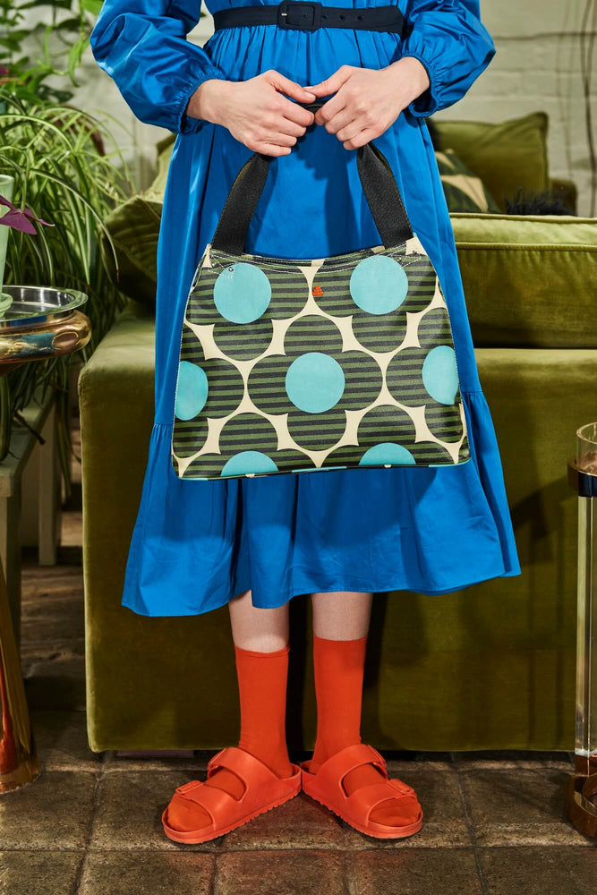 Person in blue dress and orange shoes holding a spot flower Orla Kiely bag