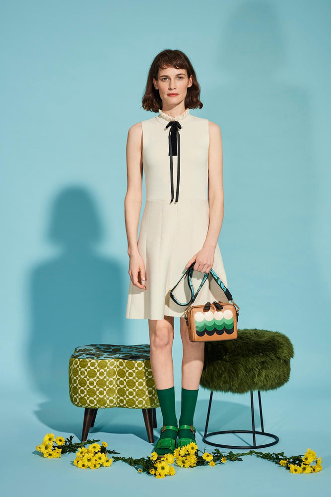 Person holding a leather Orla Kiely bag in front of a blue background