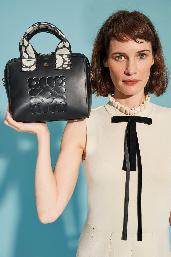 Person holding a black embossed Leather Orla Kiely bag next to her head