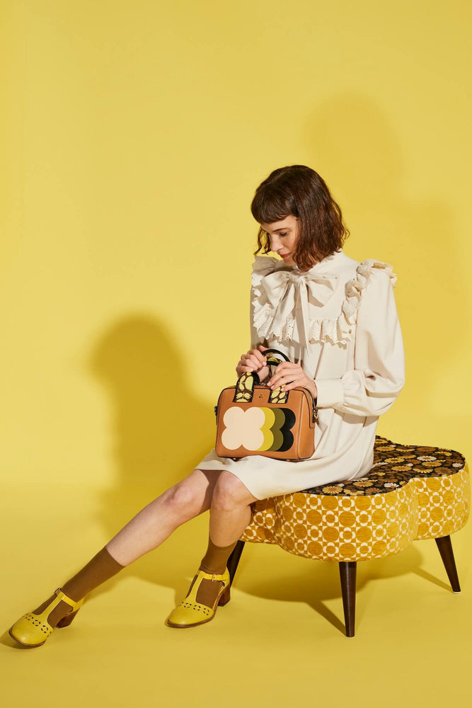 Model sitting on a yellow foot rest with a leather Orla Kiely bag 