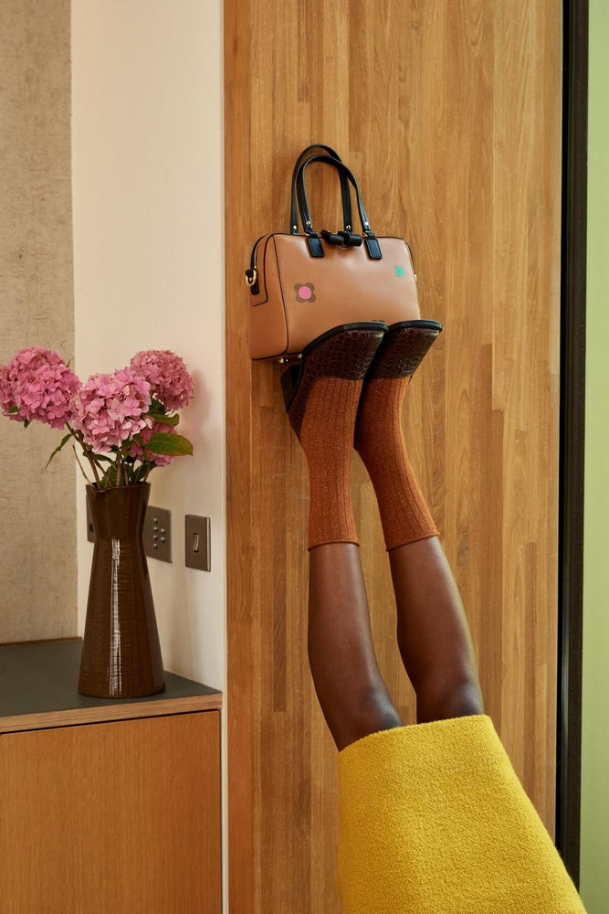 Holding a leather Orla Kiely bag up on their feet