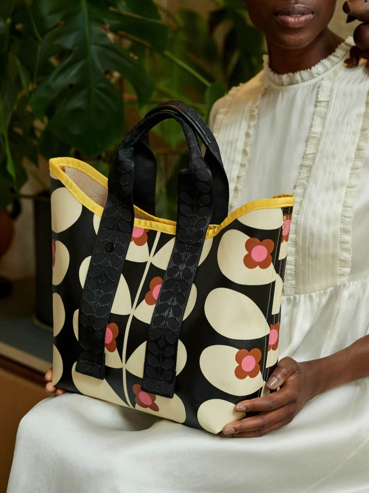 Holding a stem bloom Orla Kiely tote bag in a white dress