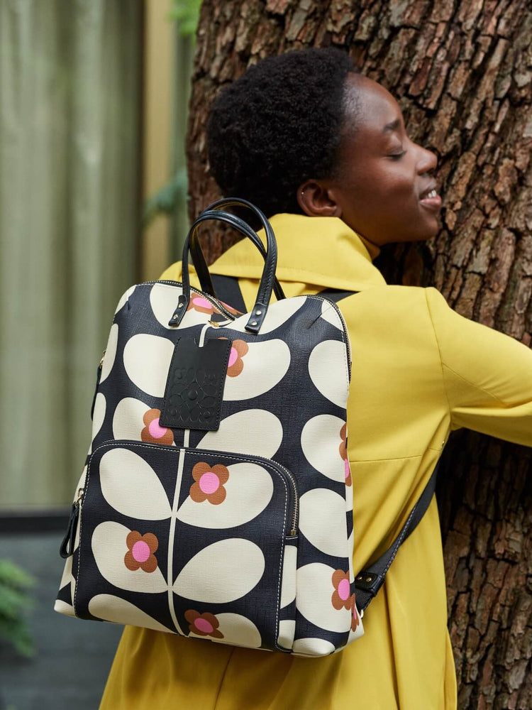 Person in yellow hugging a tree with a stem bloom Orla Kiely backpack