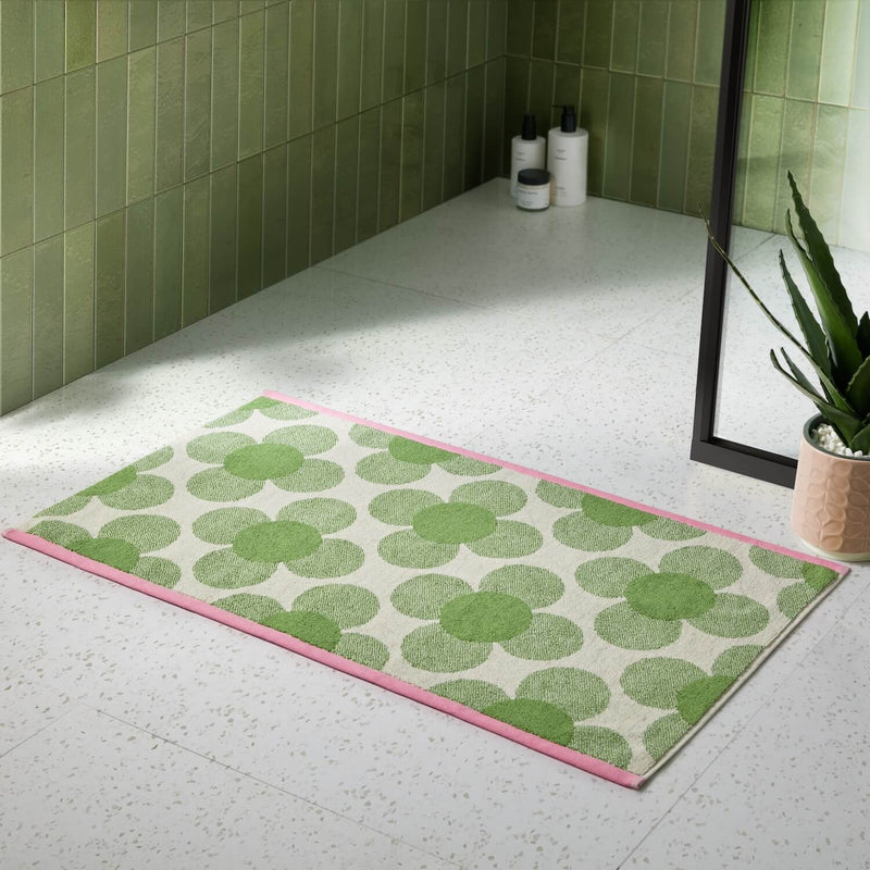 Lifestyle shot of the retro flower clover green Orla Kiely bathmat next to a shower