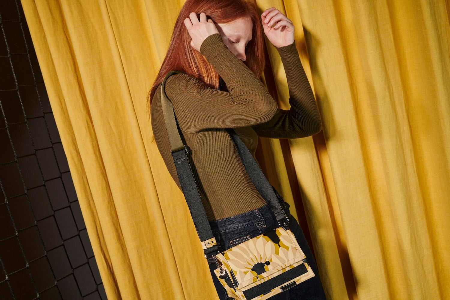 Red haired woman fixes her hair with an Orla Kiely thessaly handbag 