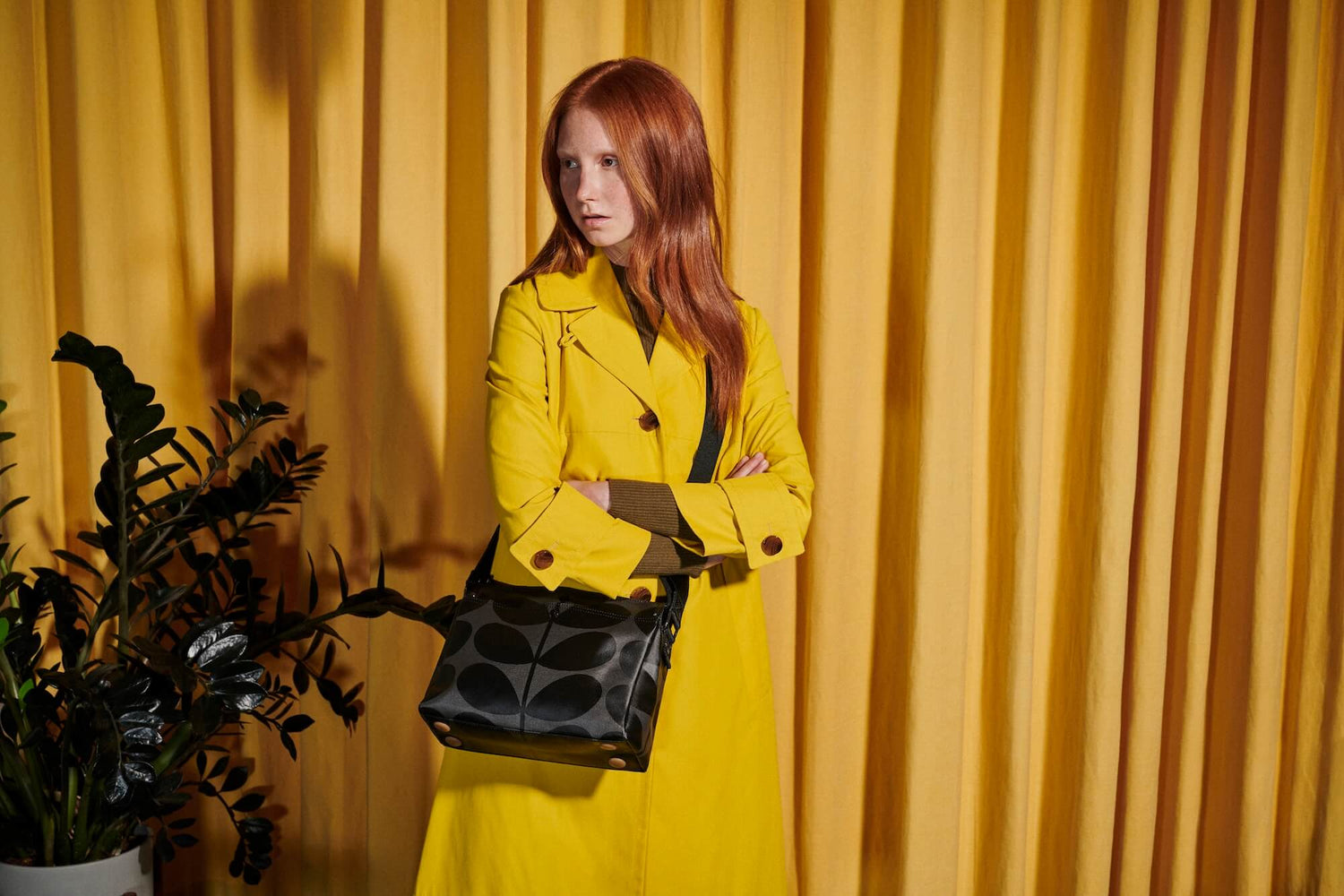 Woman in yellow next to green plant with slate Orla Kiely bag 