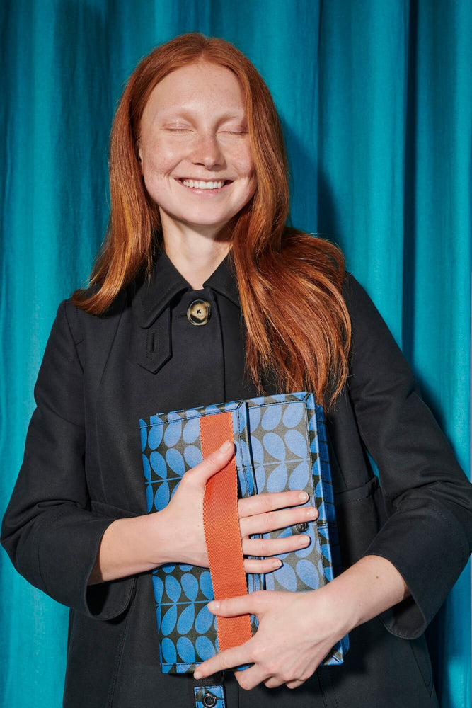 Red haired model smiling as she clutches a blue linear stem Orla Kiely bags 