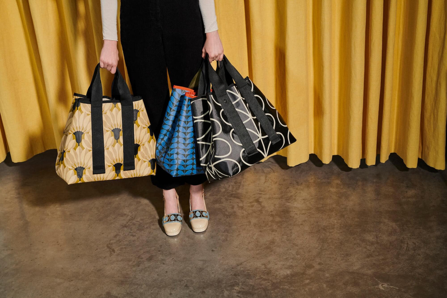 Orla Kiely totes held by a model in cream shoes