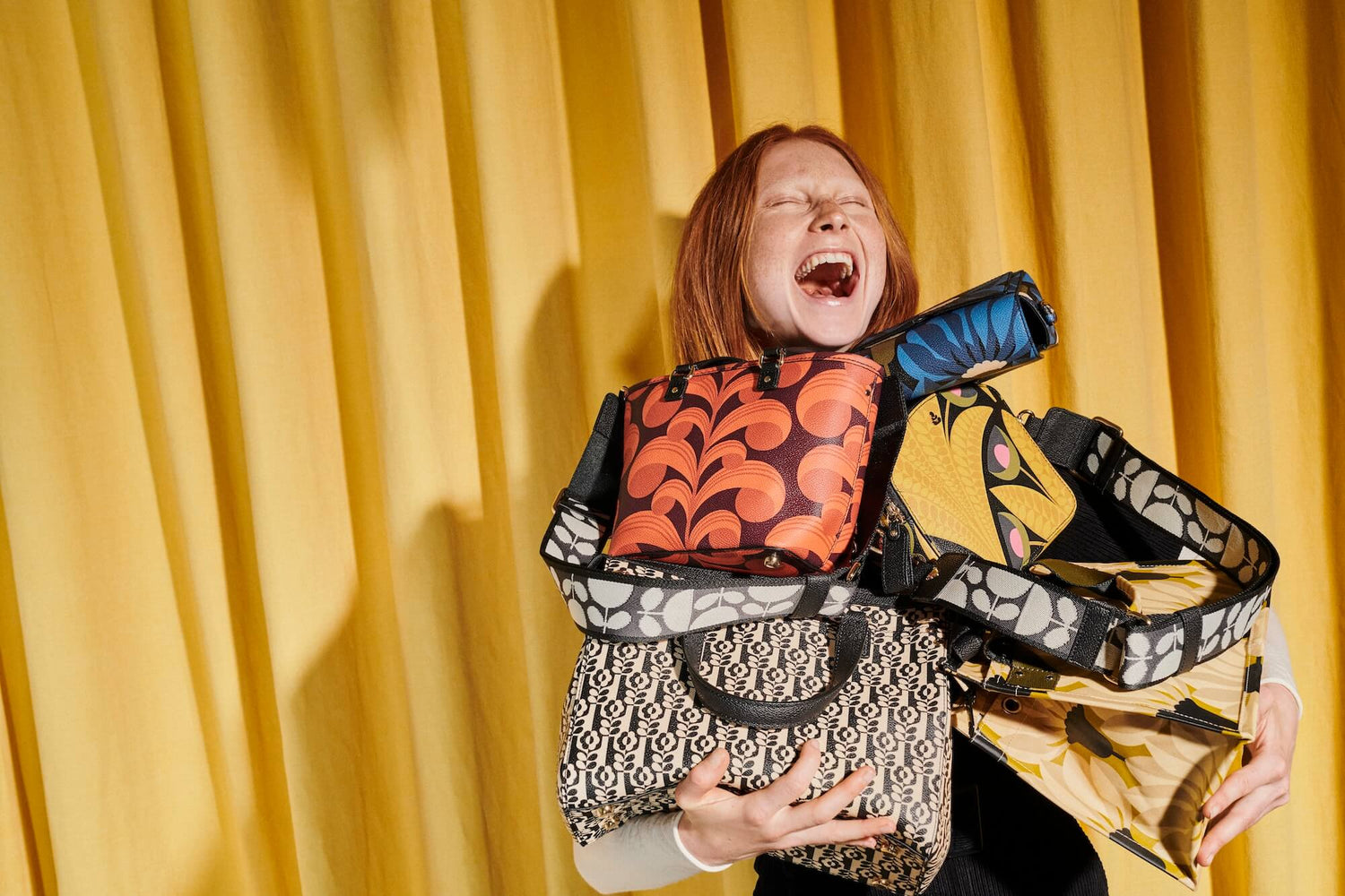 Woman gleeful about are armful of Orla Kiely handbags