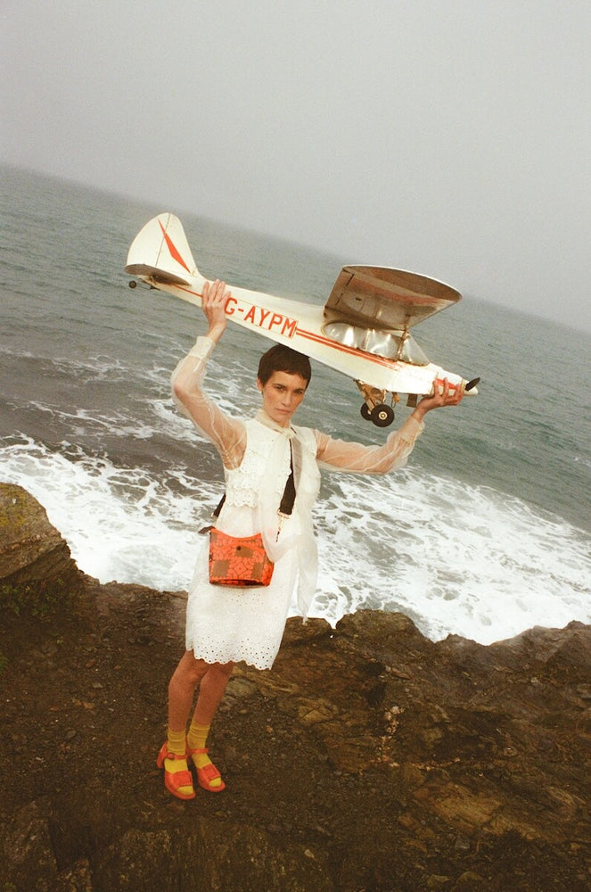 Model with Orla Kiely crossbody bag holding a plane on the beach 