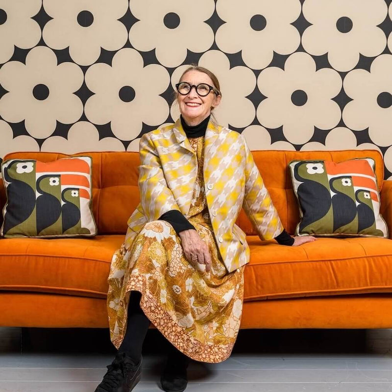 Smiling Orla Kiely sits on Orange couch with toucan cushions