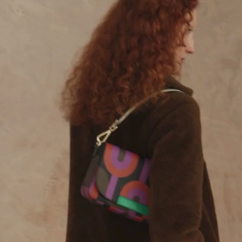 Woman in a brown coat wears a colourful  retro print handbag over her shoulder during a pohotshoot.